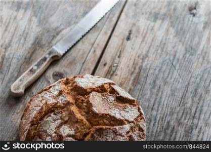 Fresh dark bread and knife on rustic cutting board, outdoors