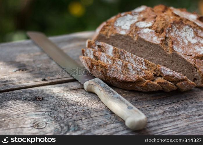 Fresh dark bread in slices. Rustic wooden cutting board and table, knife.