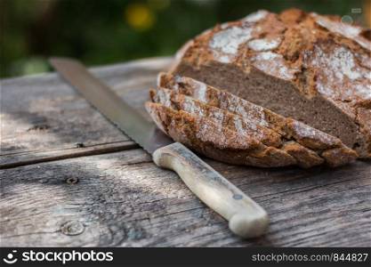 Fresh dark bread in slices. Rustic wooden cutting board and table, knife.