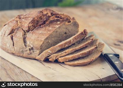 Fresh dark bread in slices. Wooden cutting board and table, knife.
