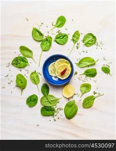 Fresh delicious baby spinach around bowl with lemon and spices on white wooden background, top view. Clean food concept.