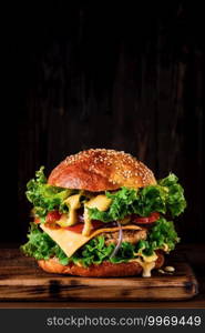 Fresh delicious grilled homemade burger with turkey cutlet with cheese, cheese sauce, and vegetables on a wooden board, on a dark background. Close up, selective focus with copy space, vertical frame