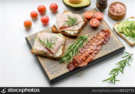 Fresh, delicious ham, butter, avocado and sesame seeds sandwiches on a wooden cutting board. Delicious healthy food. Fresh, delicious ham, butter, avocado and sesame seeds sandwiches on a wooden cutting board