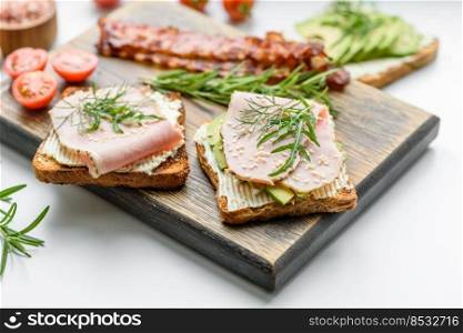 Fresh, delicious ham, butter, avocado and sesame seeds sandwiches on a wooden cutting board. Delicious healthy food. Fresh, delicious ham, butter, avocado and sesame seeds sandwiches on a wooden cutting board