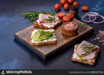 Fresh, delicious ham, butter, avocado and sesame seeds sandwiches on a wooden cutting board. Delicious hea<hy food. Fresh, delicious ham, butter, avocado and sesame seeds sandwiches on a wooden cutting board