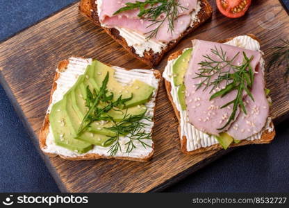 Fresh, delicious ham, butter, avocado and sesame seeds sandwiches on a wooden cutting board. Delicious healthy food. Fresh, delicious ham, butter, avocado and sesame seeds sandwiches on a wooden cutting board