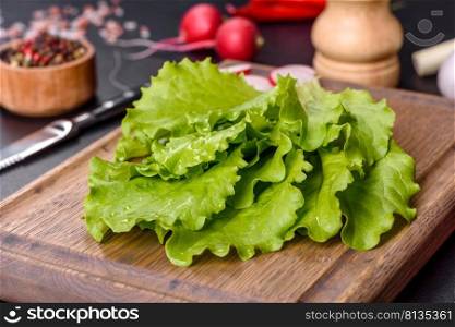 Fresh, delicious lettuce leaves on a wooden cutting board against a dark concrete background. Fresh, delicious lettuce leaves on a brown wooden cutting board