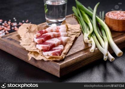 Fresh delicious pork lard with green onions on a wooden cutting board on a dark concrete background. Fresh delicious pork lard with green onions on a wooden cutting board