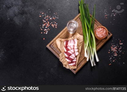 Fresh delicious pork lard with green onions on a wooden cutting board on a dark concrete background. Fresh delicious pork lard with green onions on a wooden cutting board