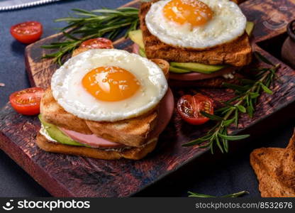 Fresh, delicious sandwiches with fried egg, ham, butter, avocado and sesame seeds on a wooden cutting board. Delicious healthy food. Fresh, delicious sandwiches with fried egg, ham, butter, avocado and sesame seeds