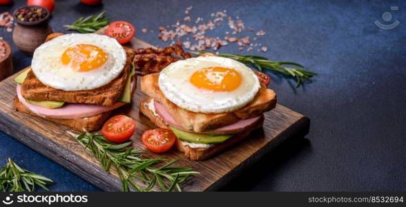 Fresh, delicious sandwiches with fried egg, ham, butter, avocado and sesame seeds on a wooden cutting board. Delicious healthy food. Fresh, delicious sandwiches with fried egg, ham, butter, avocado and sesame seeds