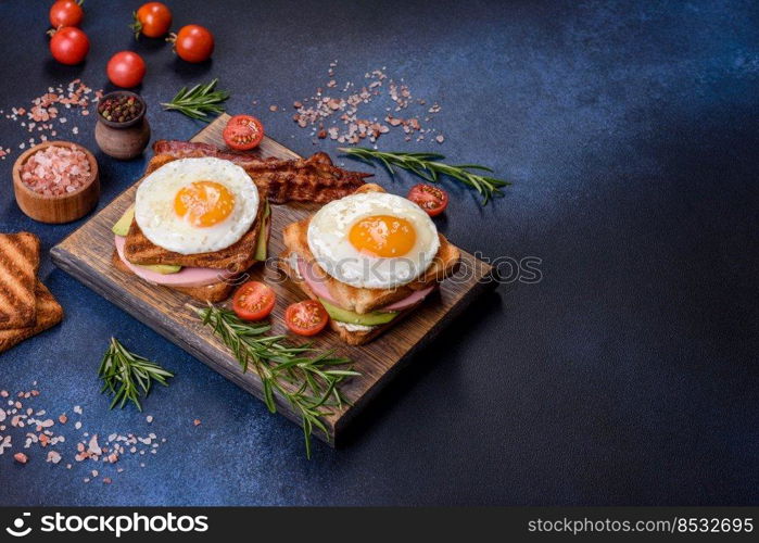 Fresh, delicious sandwiches with fried egg, ham, butter, avocado and sesame seeds on a wooden cutting board. Delicious healthy food. Fresh, delicious sandwiches with fried egg, ham, butter, avocado and sesame seeds