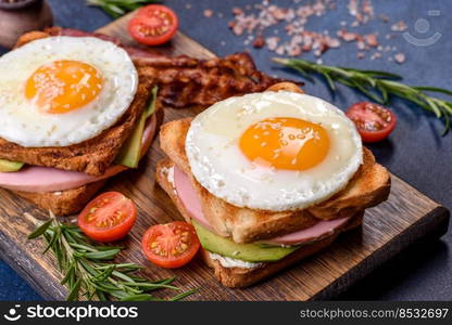 Fresh, delicious sandwiches with fried egg, ham, butter, avocado and sesame seeds on a wooden cutting board. Delicious healthy food. Fresh, delicious sandwiches with fried egg, ham, butter, avocado and sesame seeds