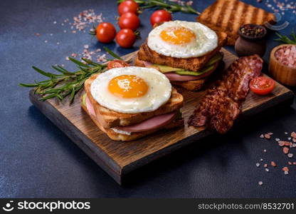 Fresh, delicious sandwiches with fried egg, ham, butter, avocado and sesame seeds on a wooden cutting board. Delicious healthy food. Fresh, delicious sandwiches with fried egg, ham, butter, avocado and sesame seeds