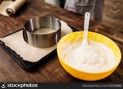 Fresh dough in the bowl and pan with parchment paper on wooden table, closeup view