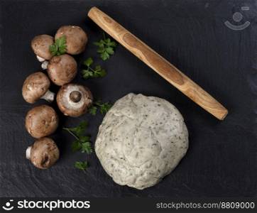 Fresh dough, mushrooms and herbs for making homemade pizza on dark stone background 