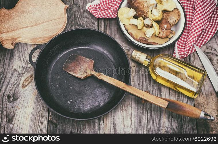 fresh edible wild mushrooms, olive oil and black round cast-iron frying pan, top view