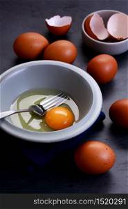 Fresh eggs and yolk in small bowl with folk on dark background. Healthy food, healthy cooking and protein food concept.