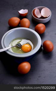 Fresh eggs and yolk in small bowl with folk on dark background. Healthy food, healthy cooking and protein food concept.