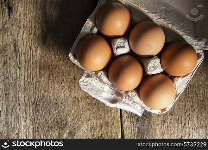 Fresh eggs in egg box in moody natural lighting vintage style set up. food, fresh, raw, fruit, vegetables, wood, wooden, background, grunge, retro, vintage, moody, dark,
