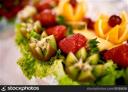 Fresh, exotic, organic fruits, light snacks in a plate on a buffet table. Assorted mini delicacies and snacks, restaurant food at event. Strawberries in a glass bowl on the white table
