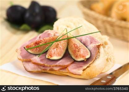 Fresh fig slices on smoked ham sandwich garnished with chives on sandwich paper with knife on the side (Selective Focus, Focus on the middle of the sandwich)