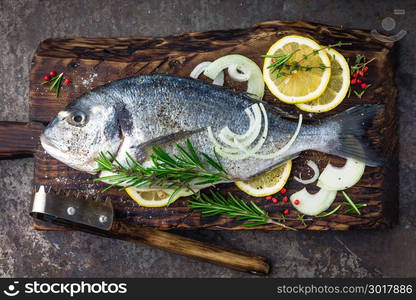 Fresh fish dorado with ingredients for cooking on wooden board. Raw sea bream or dorada fish on dark vintage metal background. Dietary food. Top view