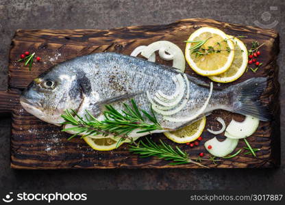 Fresh fish dorado with ingredients for cooking on wooden board. Raw sea bream or dorada fish on dark vintage metal background. Dietary food. Top view