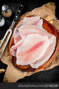 Fresh fish fillet on a wooden plate. On a black background. High quality photo. Fresh fish fillet on a wooden plate.