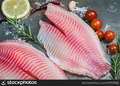 Fresh fish fillet sliced for steak or salad with herbs spices rosemary tomato and lemon / Raw tilapia fillet fish on plate and ingredients for cooking food