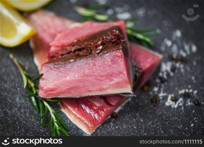 Fresh fish fillet sliced for steak or salad with herbs spices rosemary and lemon / Raw fish seafood on black plate background , Longtail tuna , Eastern little tuna fillet ingredients for cooking food