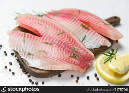 Fresh fish fillet sliced for steak or salad with herbs spices rosemary and lemon / Raw tilapia fillet fish and salt on white stone background and ingredients for cooking food