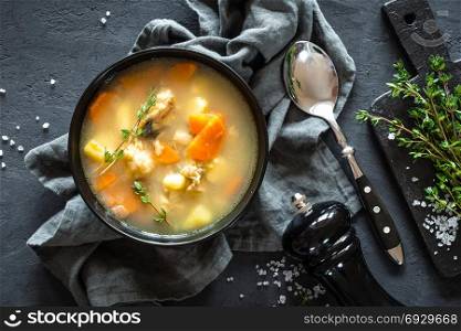 Fresh fish soup in bowl on dark background, top view
