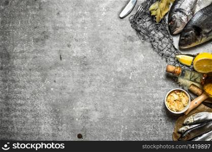 Fresh fish with lemon and spices on a fishing net. On a stone background.. Fresh fish with lemon and spices on a fishing net.