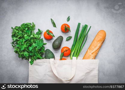 Fresh food  french baguette, avocado, tangerines, fresh parsley and young onions in a beige cotton bag on a light gray cement background, flat lay close-up. Healthy food and ecology concept.. Fresh food  french baguette, avocado, tangerines, fresh parsley and young onions in a cotton bag.