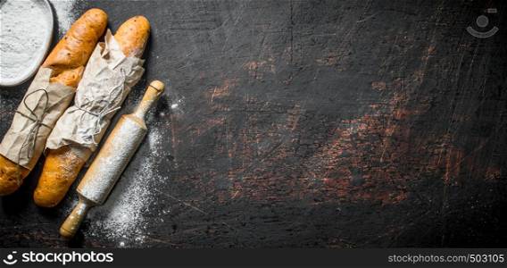 Fresh French baguette with flour and rolling pin. On dark rustic background. Fresh French baguette with flour and rolling pin.