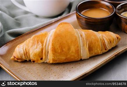 Fresh french croissants with chocolate on plate, honey, and tea