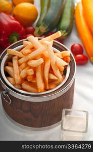 fresh french fries on a wood bucket with white dip sauce and fresh vegetables on background