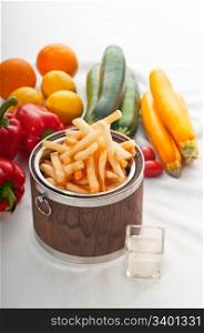 fresh french fries on a wood bucket with white dip sauce and fresh vegetables on background