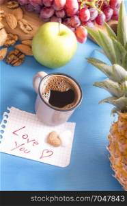Fresh fruits and nuts on a blue wooden table, cup of Arabic coffee and a paper note with love you message and heart shaped sugar on it.