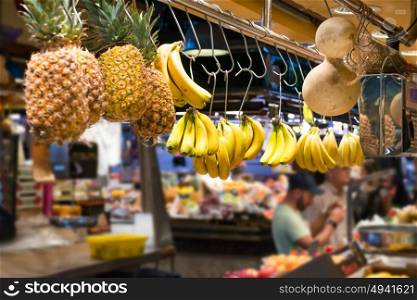 Fresh fruits bananas and pineapple hanging at food market with crowds of people