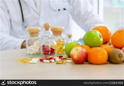 Fresh fruits, capsules and vitamins on desk.  Nutritional expert with stethoscope around neck developing dietary plan to improve eating habits of patient