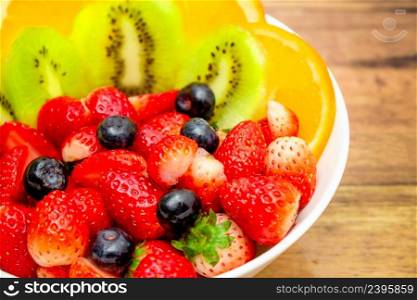 Fresh fruits concept, Fruits salad consist of kiwi and assorted berry in bowl on wooden background.