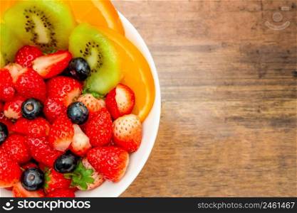 Fresh fruits concept, Fruits salad consist of kiwi and assorted berry in bowl on wooden background.