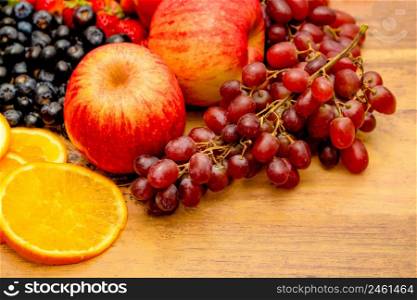 Fresh fruits concept, Healthy fruits consist of grapes apple orange and berry on wooden background.