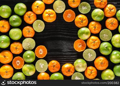 Fresh full oranges, lime, and halves fruits on black wooden background with copy space