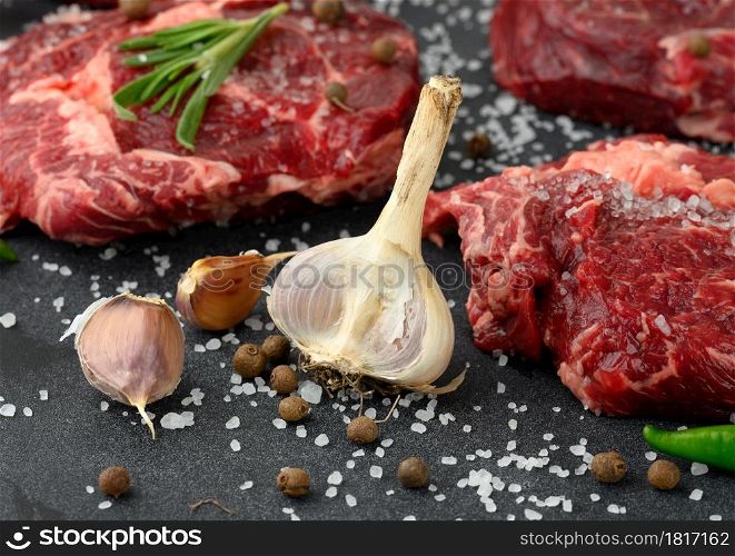 fresh garlic andraw piece of beef ribeye with rosemary, thyme on a black table, close up