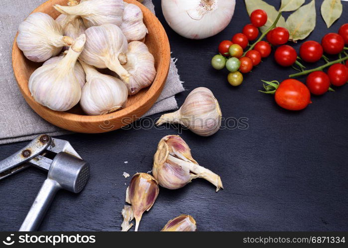 Fresh garlic in a wooden bowl, near a bunch of red cherry tomatoes