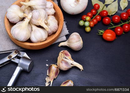 Fresh garlic in a wooden bowl, near a bunch of red cherry tomatoes