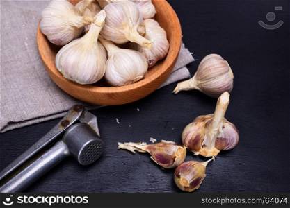 Fresh garlic in the husk and in a wooden bowl on a black background with an iron garlic press